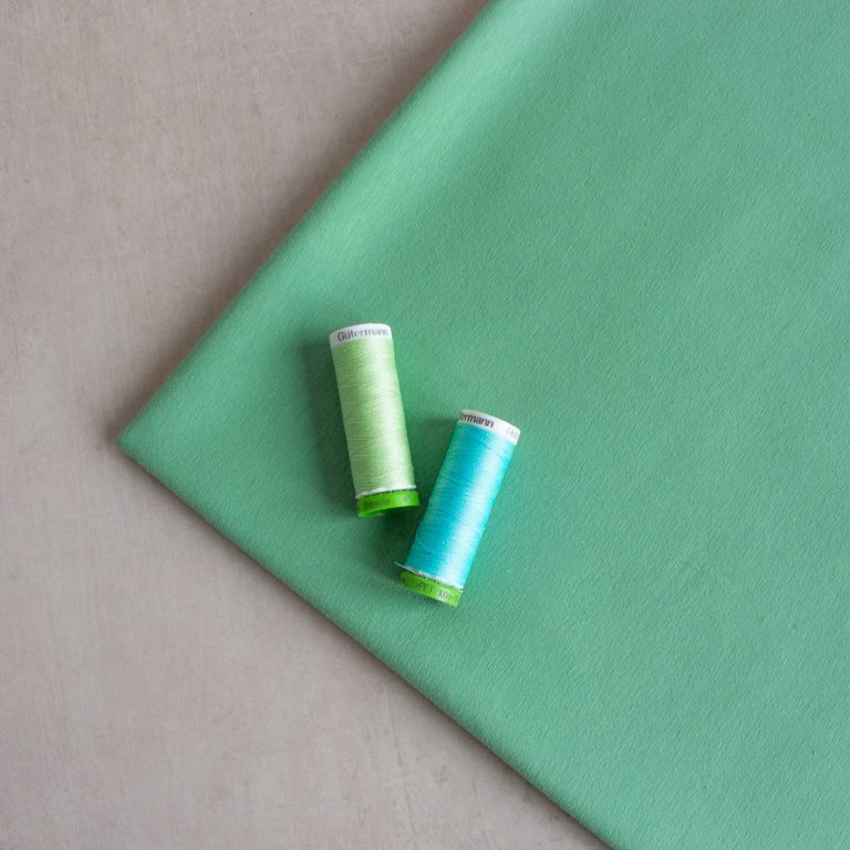 organic cotton jersey fabric in aqua green, view from the top with two threads placed on top