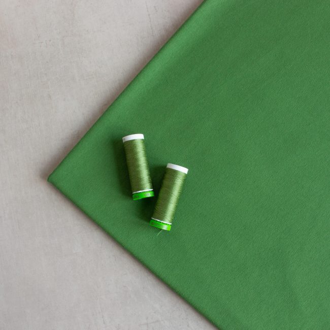 organic cotton jersey fabric in garden green, view from the top with 2 matching threads placed on top