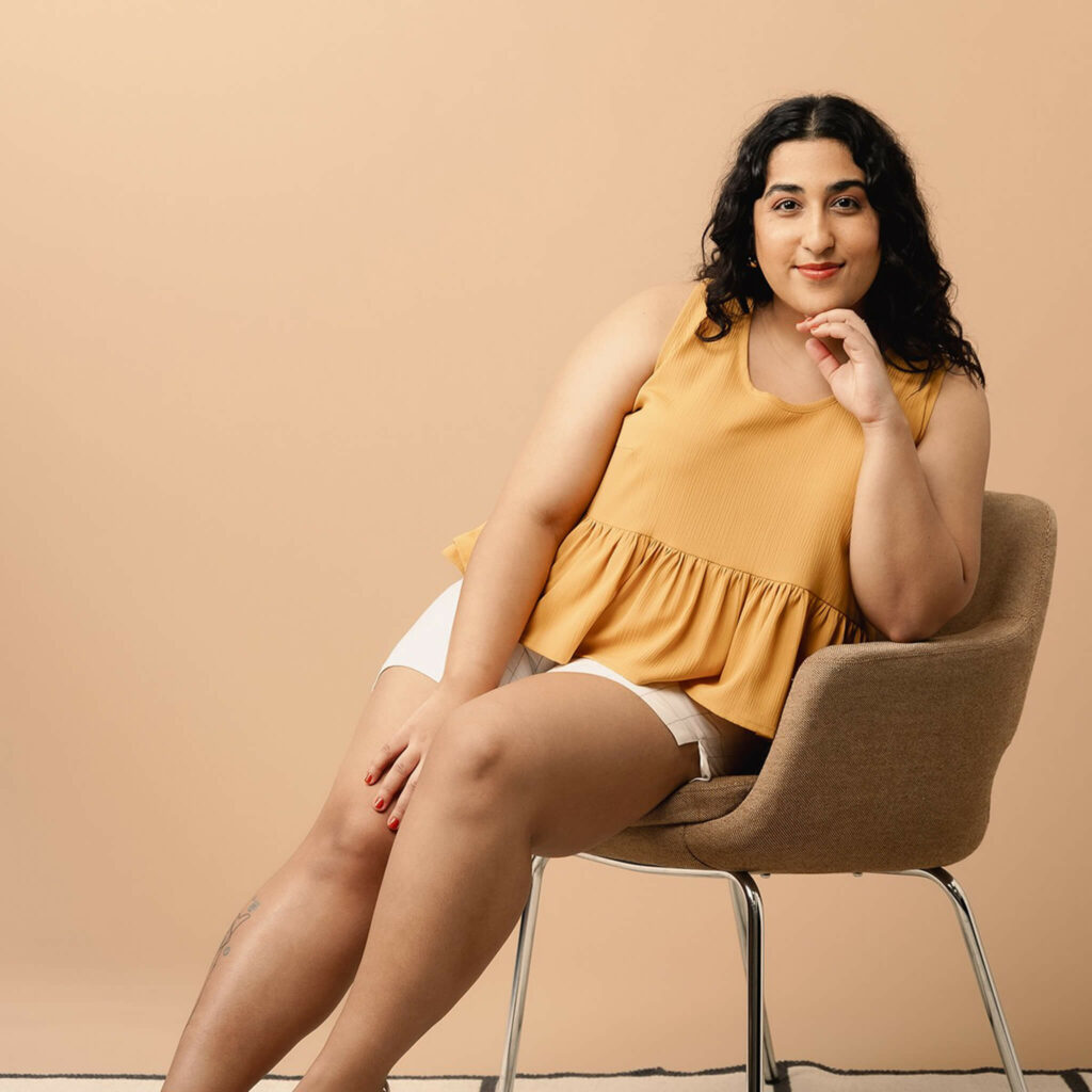 model wearing yellow top, sitting on a chair
