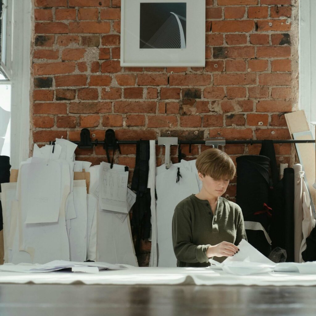 seamstress standing in front of a cutting table, handling paper sewing patterns